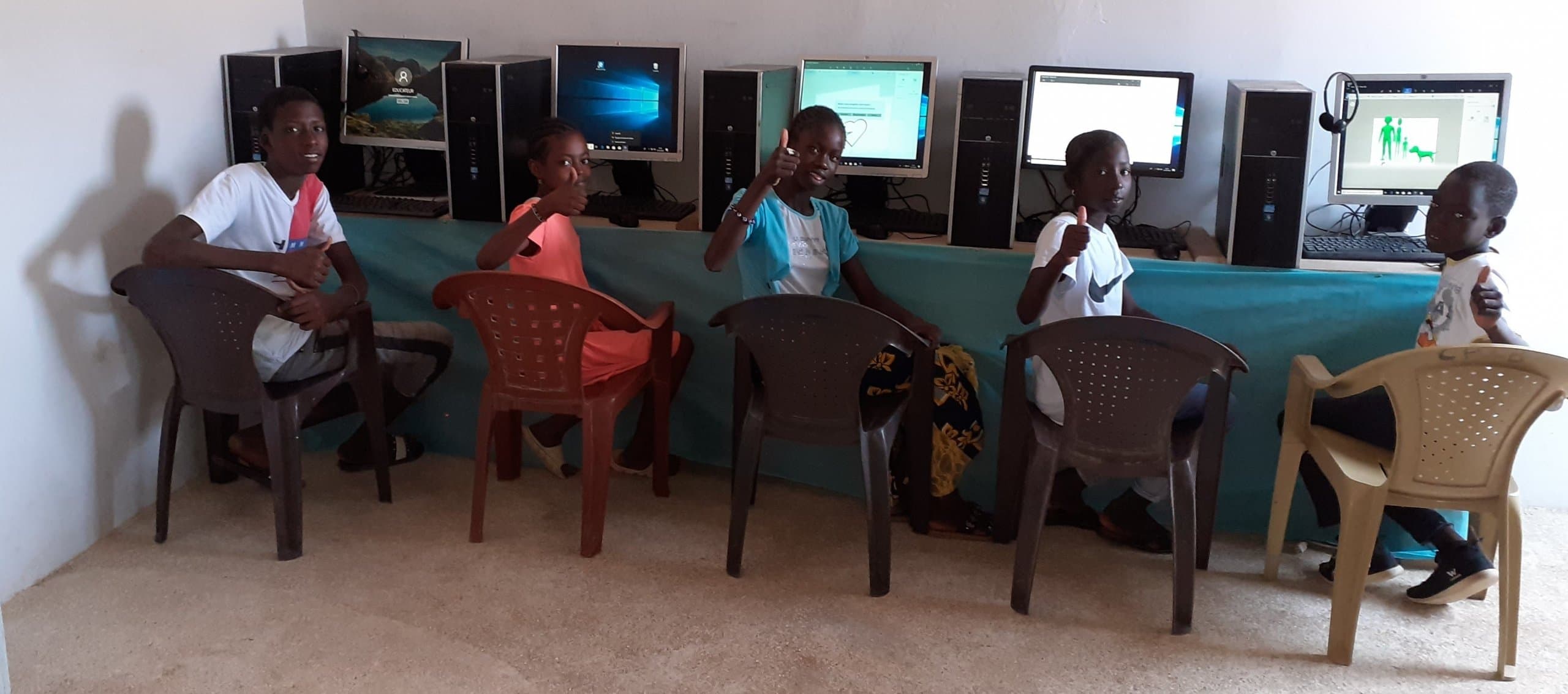 Children sitting in front of computers in the new computer lab, smiling and giving thumbs up